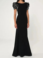 Model wearing a black round neck maxi dress with ruffle sleeves, standing in a clean studio setting.