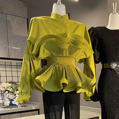 Green ruffled blouse on a mannequin with a black dress in the background.
