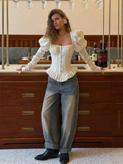 Outfit view focusing on the ruffled peplum hem and fitted waist of an ivory corset blouse paired with denim jeans.