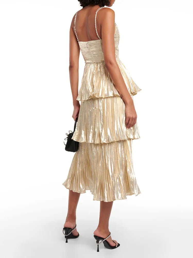 Shimmering gold-toned pleated dress featuring a fitted bodice and layered frill skirt on a studio background.