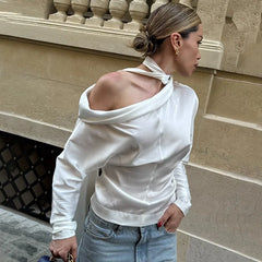 A woman wearing an autumn fashion shirring detail blouse in white for women and blue jeans against a beige wall.