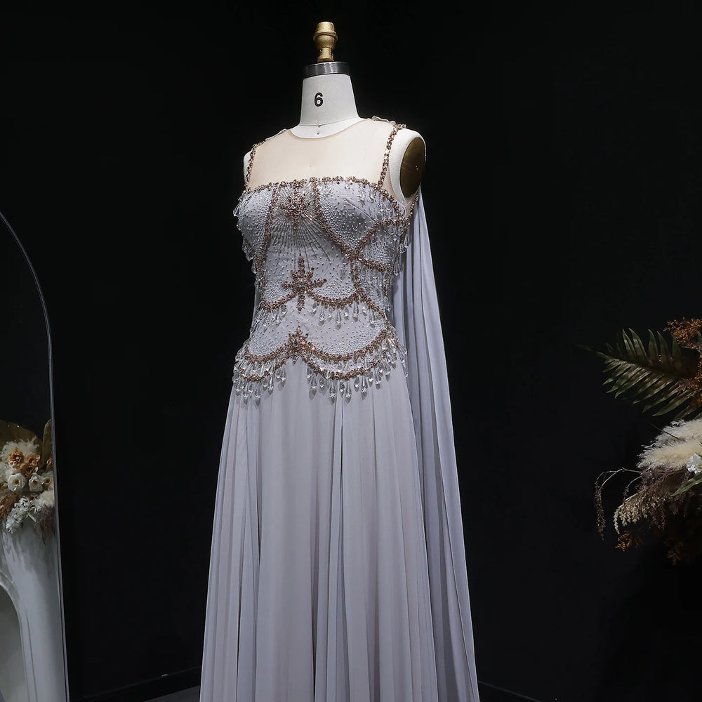 Cape sleeve formal gown with embellished top and soft tulle drape against a dark backdrop