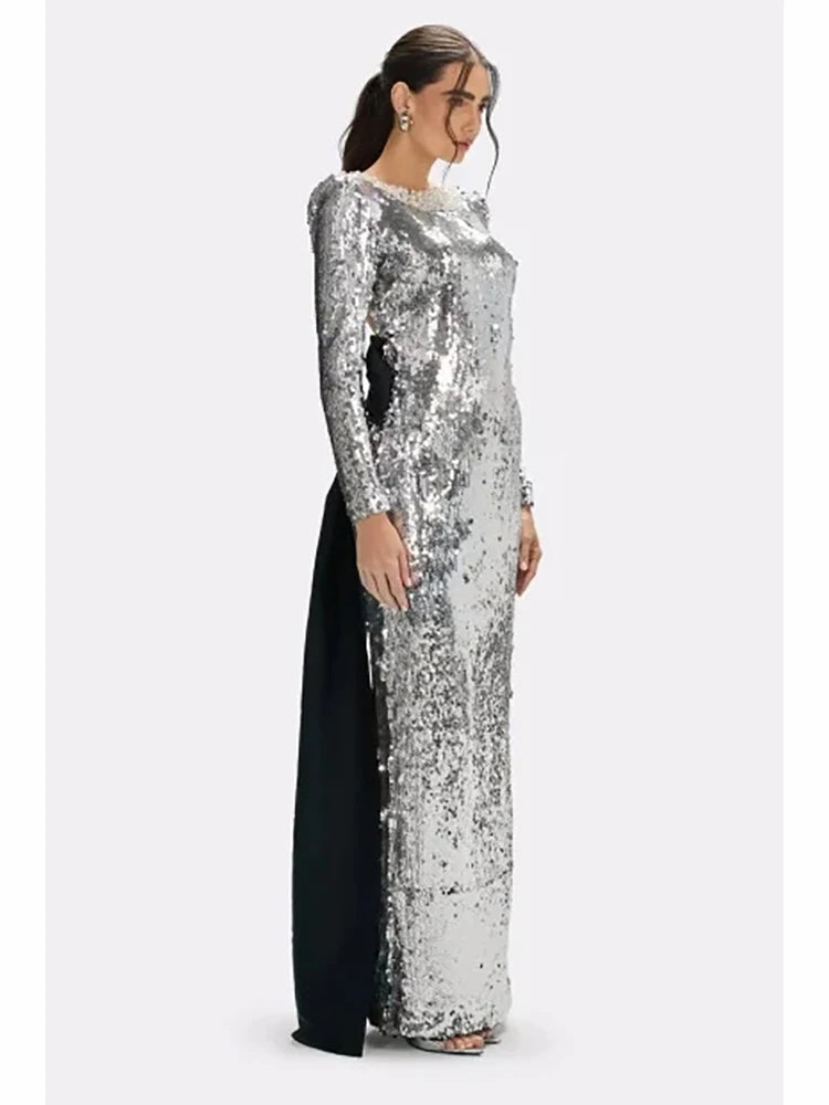 Rear angle highlighting the open-back cut and bow detail on a silver sequin maxi dress, styled for an evening event silhouette.