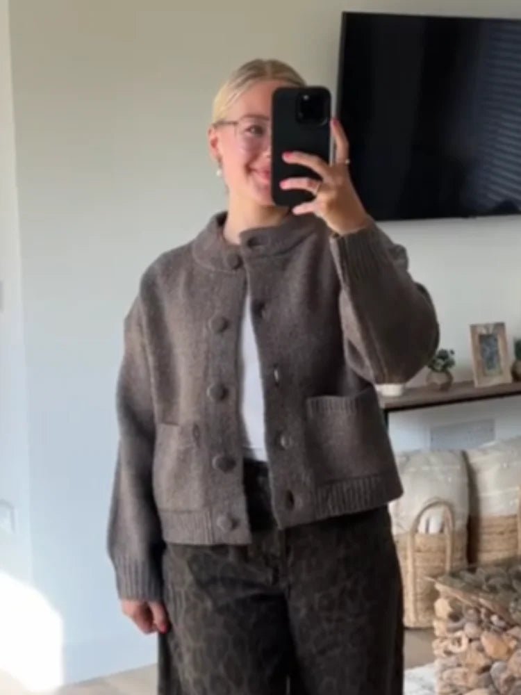 Person wearing a brown knitted jacket taking a mirror selfie.