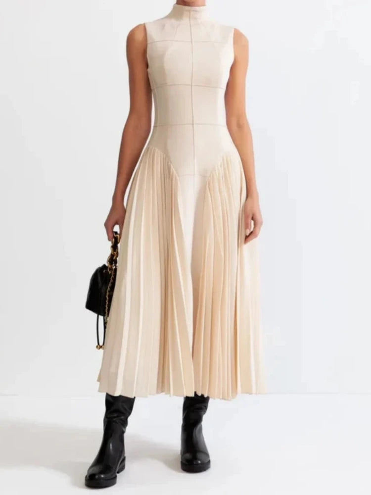 Beige sleeveless pleated dress paired with black boots on white background