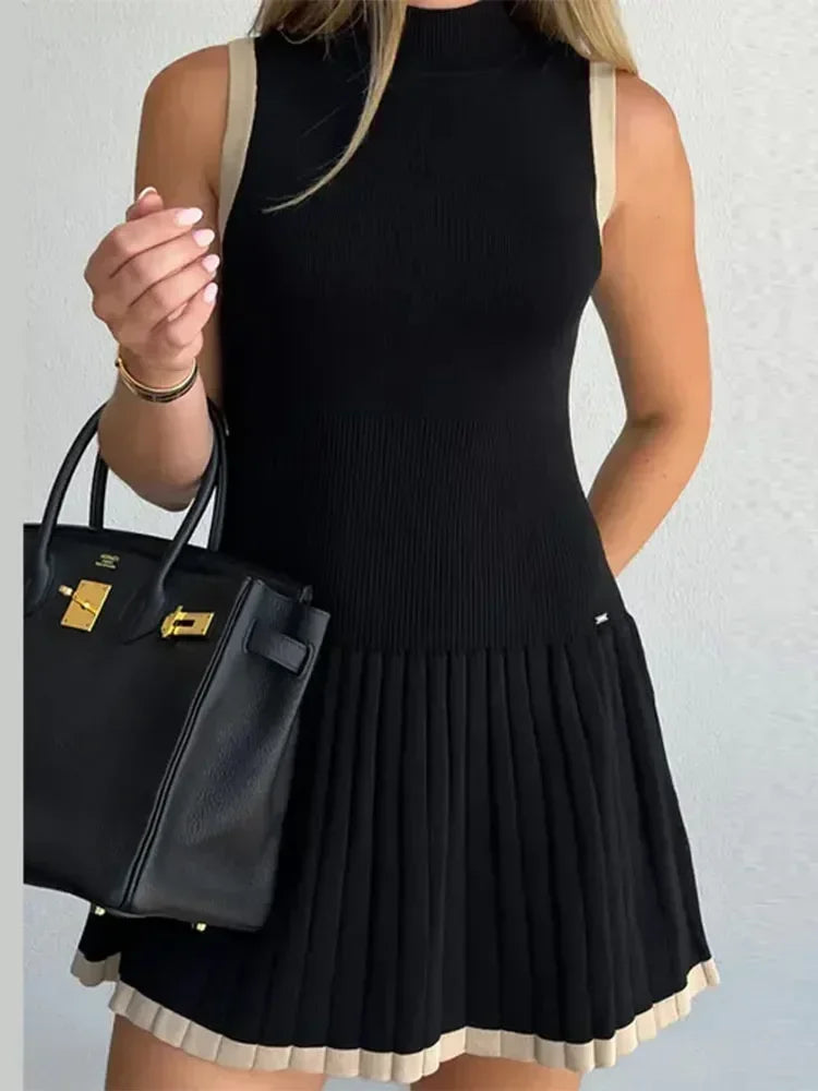 Woman wearing a black dress holding a black handbag against a light gray background