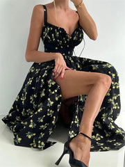 A woman wearing a sleeveless black floral maxi dress with a slit sitting on a white surface.