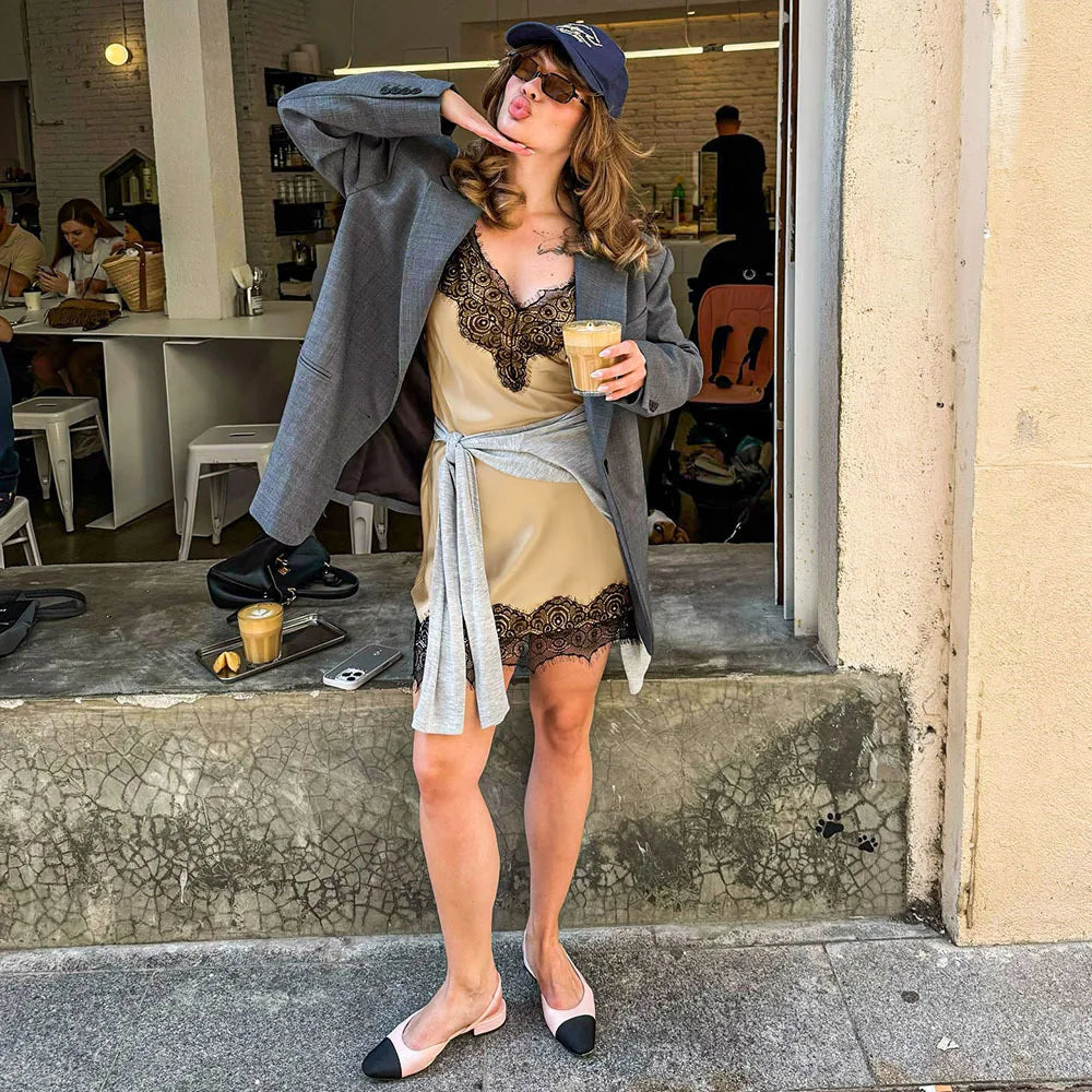 Woman in a casual setting holding a drink, wearing a coat over a dress with lace details.