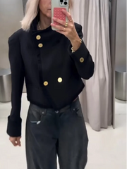 Indoor styling view of a black structured cropped jacket with metal button accents, designed for polished day-to-night layering.