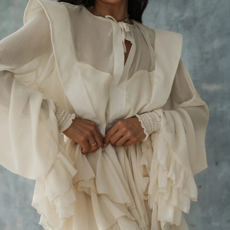 Person wearing an apricot chiffon mini dress with a tiered hem and soft pastel tone against a grey background