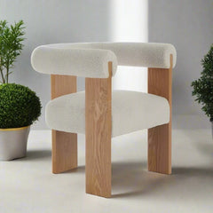 A solid wood dining chair with a cream-colored padded backrest and seat, positioned in a room with plants and a wooden floor.