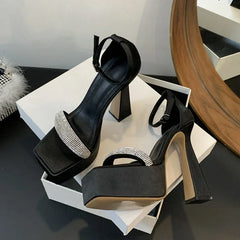 Black high-heeled shoes with rhinestone details on a white surface.