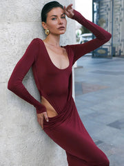 A woman in a square-neck, backless party dress in burgundy for women’s evening wear, leaning against a textured wall.