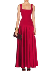 Model wearing a square neck maxi dress with a fitted bodice and flowing skirt, styled with a clutch against a clean studio backdrop.