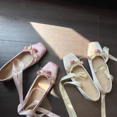 Pair of pink and white flat shoes with decorative elements on a dark wooden floor.