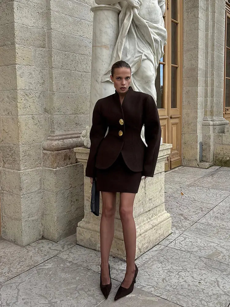 Close-up showing the stand collar and button front of the deep brown jacket, highlighting the structured tailoring and clean neckline.