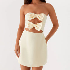 A woman modeling a strapless bow mini dress with a cutout back.