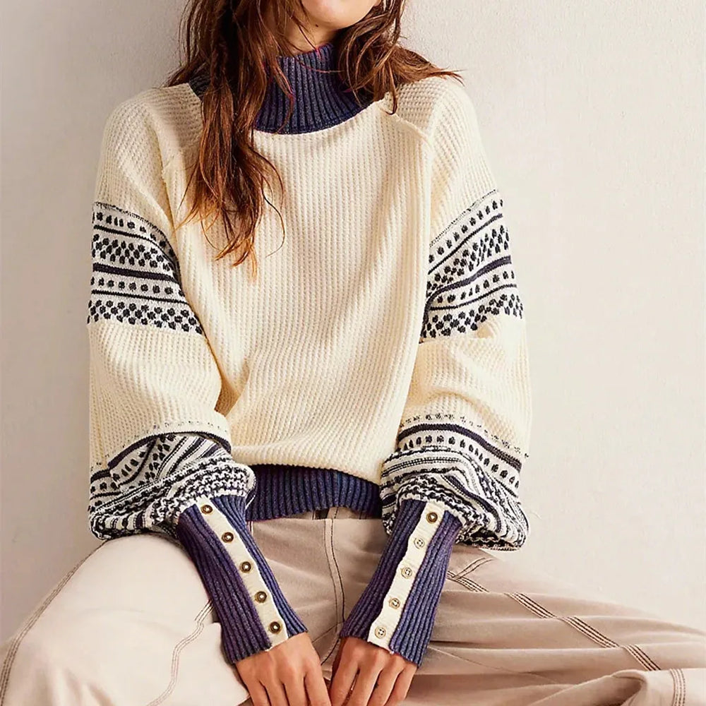 Model seated wearing a crew-neck knit sweater with striped statement sleeves and ribbed trims styled with tailored trousers.