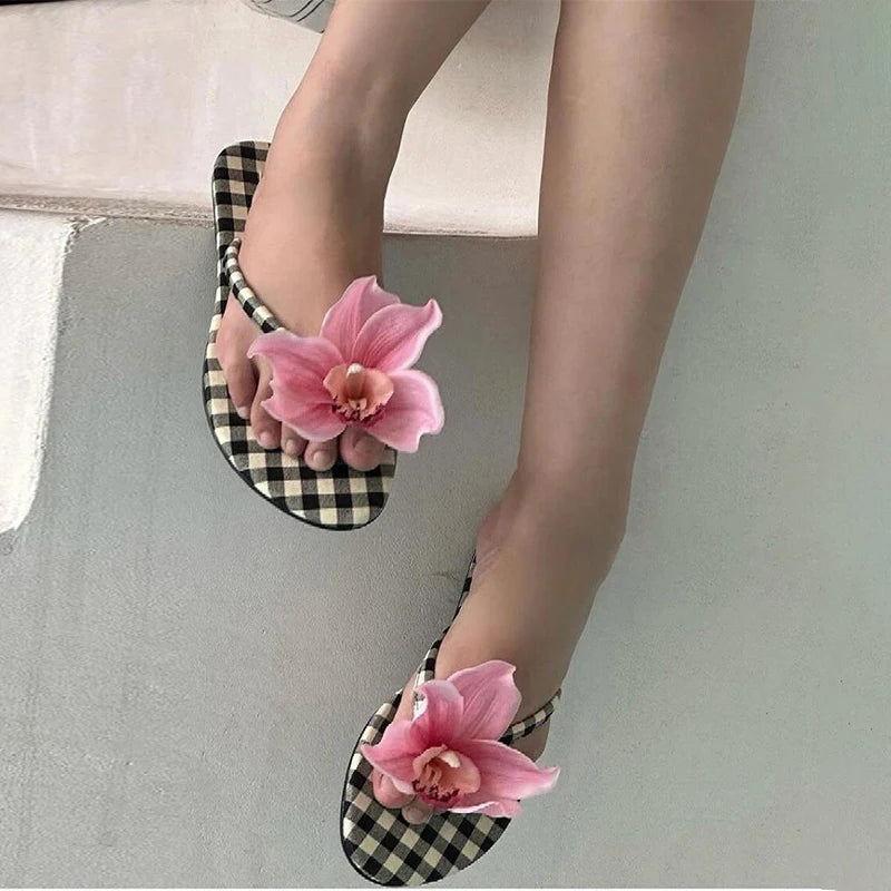 Checkered flip-flops with pink flowers worn on a neutral background
