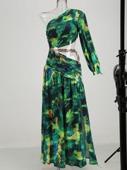A mannequin  displaying a floral printed one-shoulder chain maxi dress with green-tone chain detail and a side hollow detailing.
