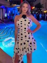 Woman in a vacation-ready polka dot mini shown in a lightweight, flouncy fit standing by a pool at night.