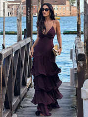 Full-length outdoor shot showing the flowing tiered ruffles and soft satin drape of the burgundy maxi dress near boats and water.