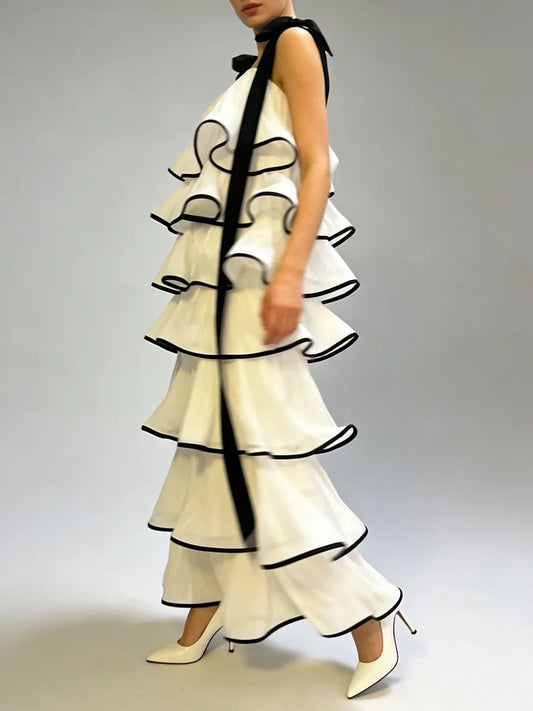 Model walking in a light maxi dress with layered ruffle tiers and dark contrast trim, sleeveless square neckline and shoulder bow detail