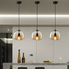 Three pendant ceiling lights with a black frame and clear glass shades hang over a white dining table with bottels and glasses on it, in a room with gray walls.