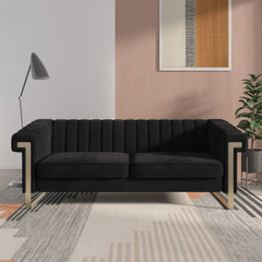 A black velvet long couch Chesterfield sofa with a chaise, displayed in a room with a light brown wall and a framed abstract picture above it, with a lamp overlooking the sofa.