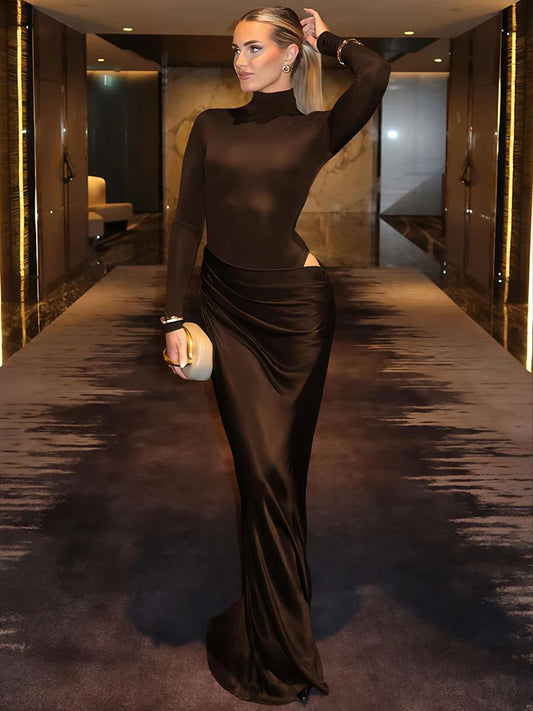 Woman in a long-sleeve turtleneck ruched maxi dress in blackstanding in a modern interior setting.