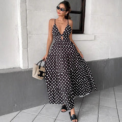 Close-up of a woman wearing a black and white polka dot dress holding a straw bag against a grey wall.
