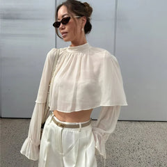 Street-style look with flowing white cape blouse, semi-sheer long sleeves, and tailored trousers for an effortless day-to-evening outfit.