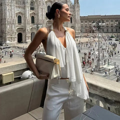 Model in a white halter mesh top with layered irregular hem, styled on a terrace overlooking a busy cathedral square.