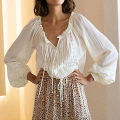 A woman wearing a white long-sleeved cotton blouse with a V-neck and lace details, paired with a leopard print skirt.
