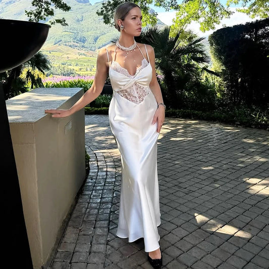 Woman in a white lace sling high waist maxi dress styled for evening parties outdoors standing outdoors with scenic background