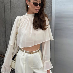 Relaxed white chiffon top styled with high-rise pants and sunglasses, balancing a minimal silhouette with a softly dramatic neckline.