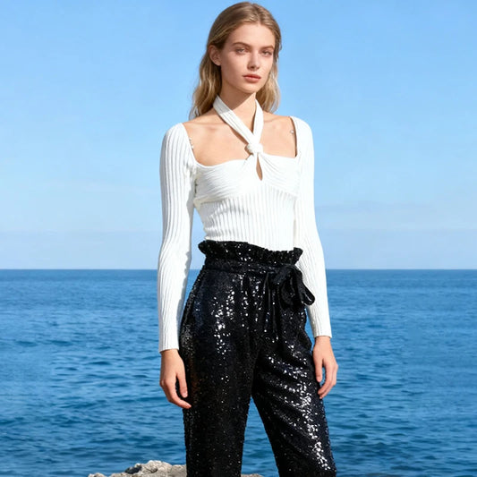 Model wearing a white rib-knit long sleeve top with twist halter neckline and keyhole cutout, styled outdoors by the ocean.