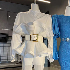 White outfit with a gold belt on a mannequin, with a blue dress in the background.