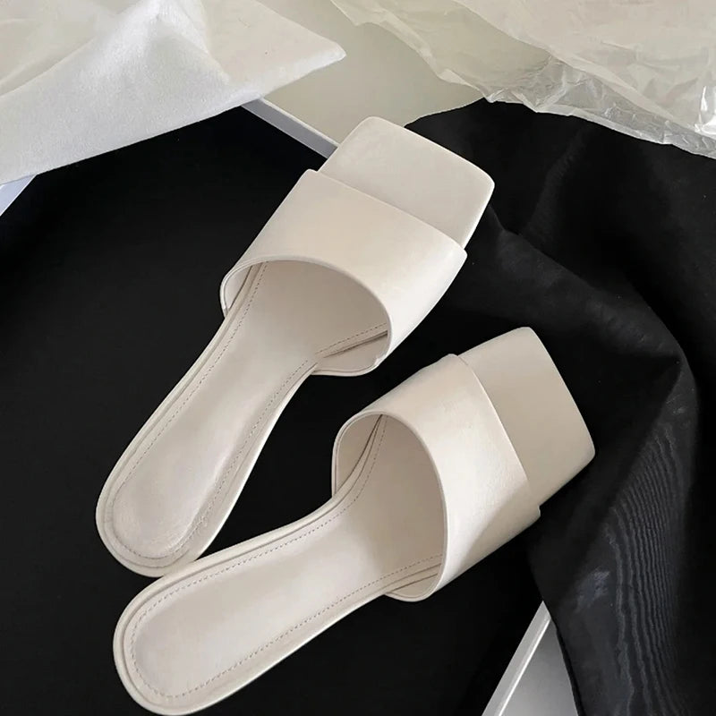 White square toe wedge heel slides placed on black fabric