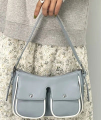 Gray crossbody bag held by a person wearing a gray sweater and floral skirt.