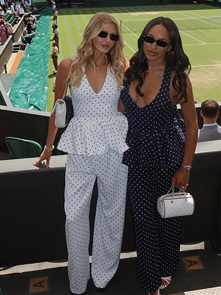 Two women  wearing white polka dot tank and wide-leg pants standing on a tennis court.