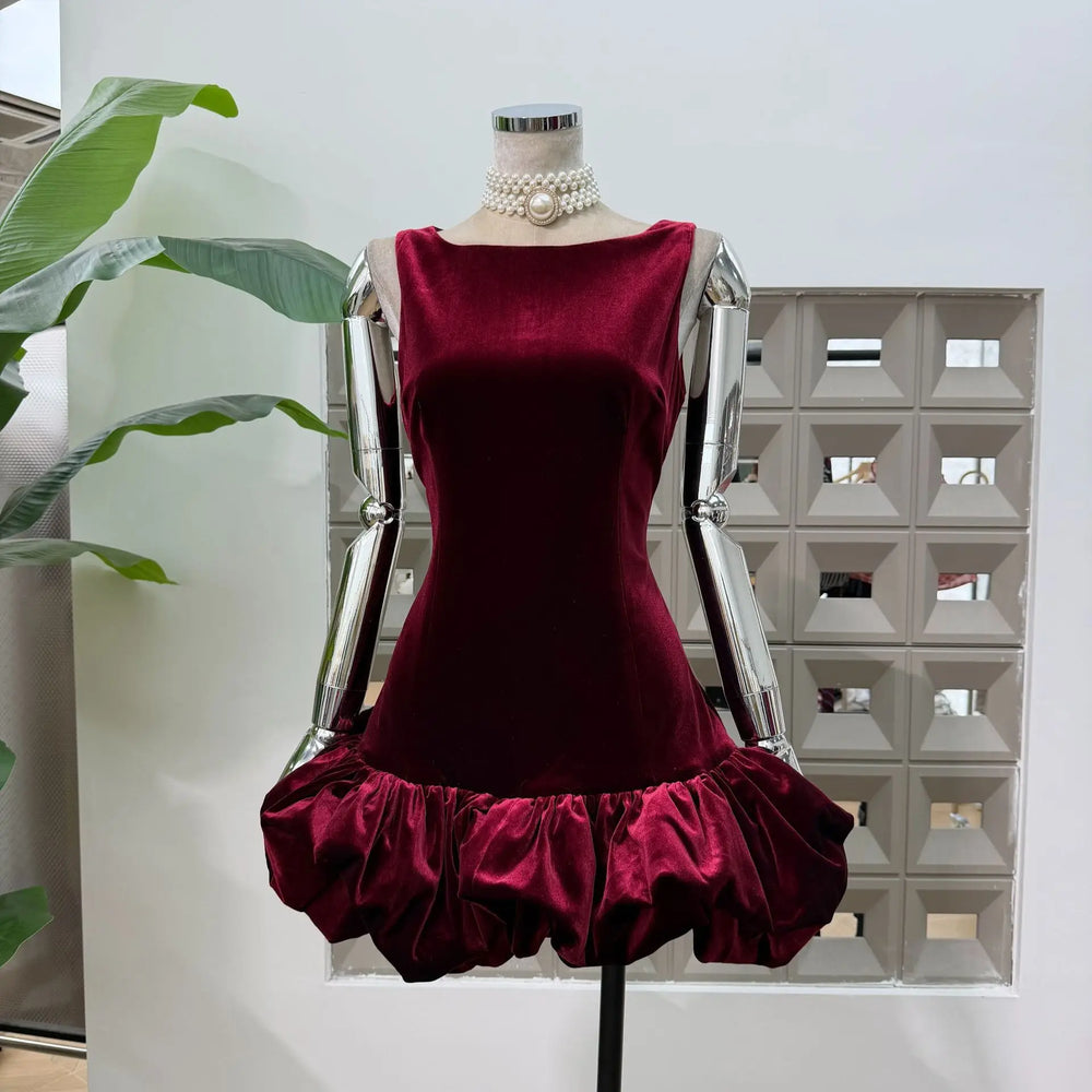 Mannequin wearing a wine-toned velvet sleeveless mini dress with a dramatic cloud bubble hem in a bright studio setting.
