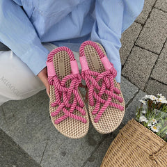 Pink woven sandals worn by a person sitting on a stone pavement.