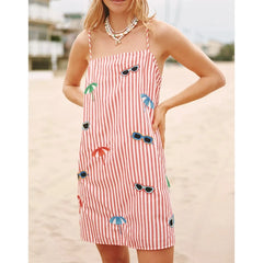 A woman wearing a Y2K striped mini dress with sunglasses, print styled for the beach, with sunglasses and palm tree patterns on a beach.