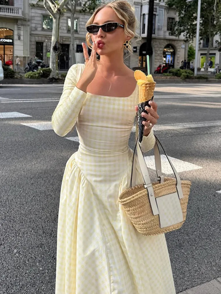 Woman in a yellow plaid maxi dress styled for autumn city strolls, eating ice cream on a city street