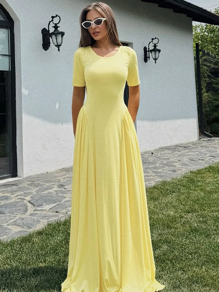A woman wearing a Yellow pleated maxi dress, styled outdoors with sunglasses, standing outdoors on a stone path.