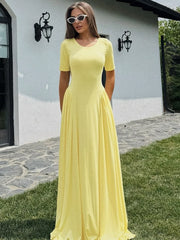 A woman wearing a Yellow pleated maxi dress, styled outdoors with sunglasses, standing outdoors on a stone path.