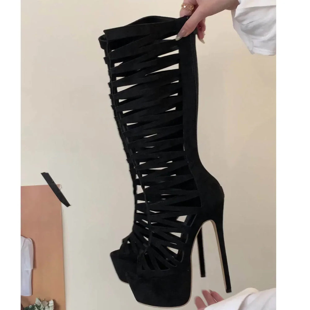 Black high-heeled boot with strappy design held by a hand against a neutral background