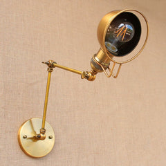 A brass adjustable swing arm wall light sconce with a gold finish and a shade, mounted on a wall with a round bulb.
