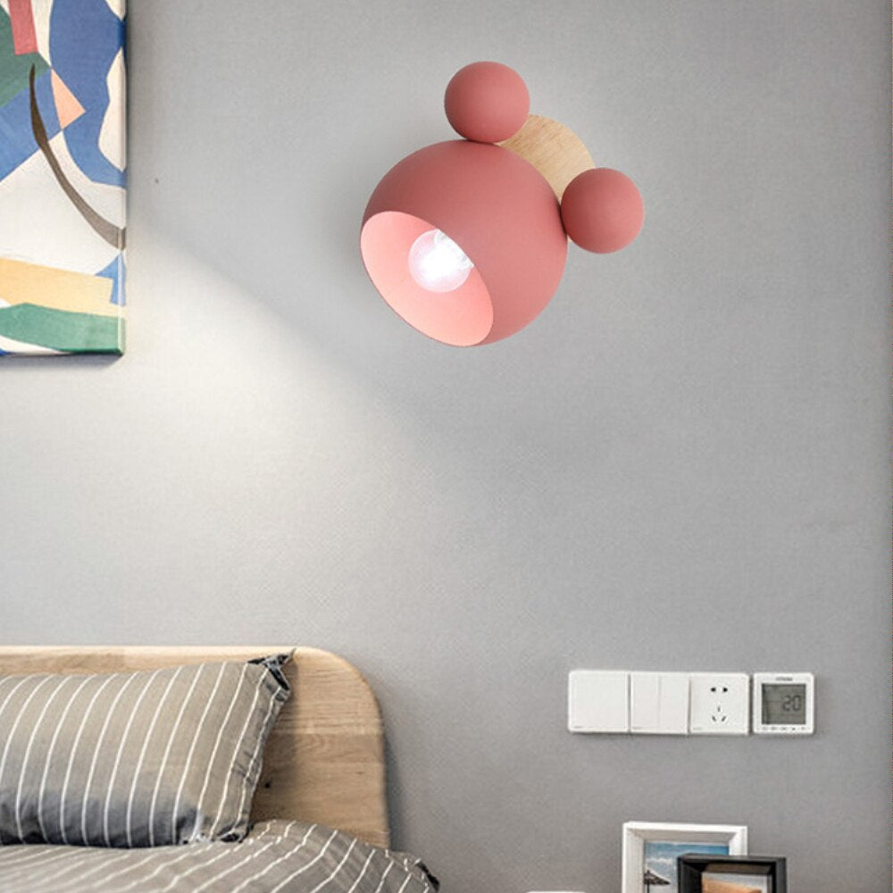 A  Mickey Mouse style Pink wall sconce with E27 sockets attached to a wall over  a bed.